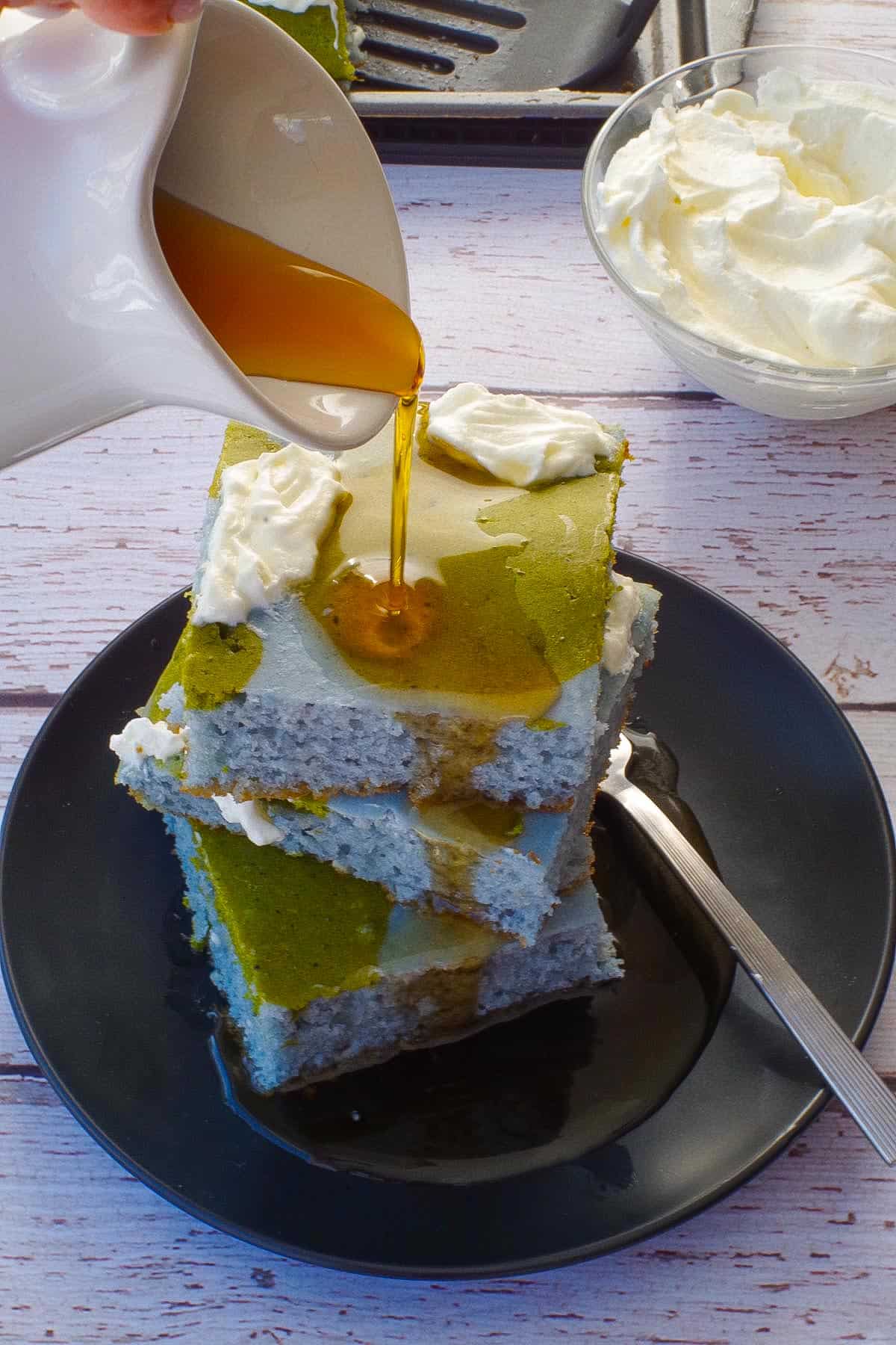3 Fluffy Sheet Pan Earth Day Pancakes stacked on a black plate with syrup being poured over them.