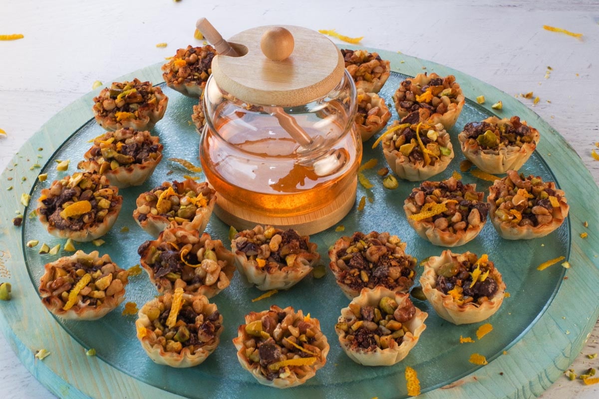 Baklava Cups on a blue glass and wooden powder with a jar of honey in the middle.