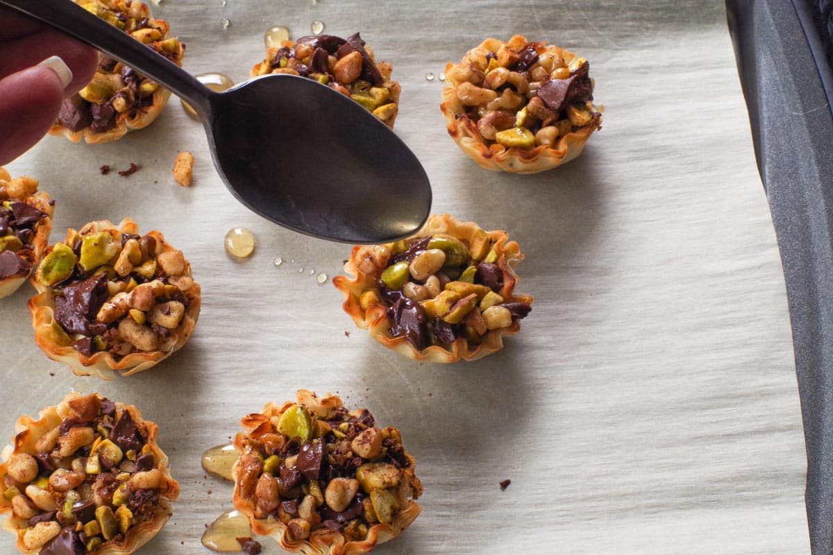 Chocolate Baklava Cups being drizzled with syrup from a small spoon.