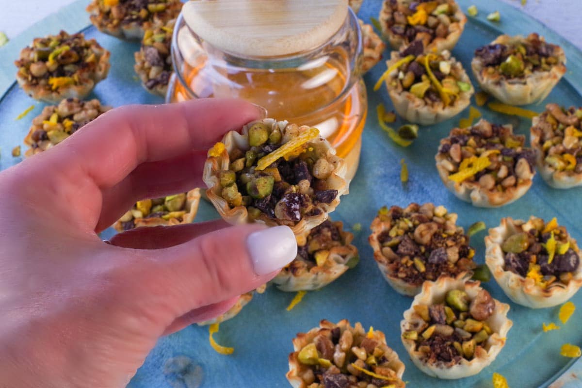 Hand holding up Chocolate Baklava Bite with honey and more Baklava Bites in the background.