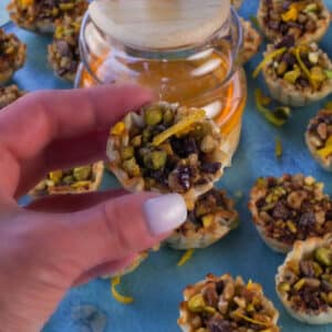 Hand holding up Chocolate Baklava Cup with honey and more Baklava Cups in the background.