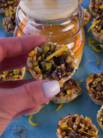 Hand holding up Chocolate Baklava Cup with honey and more Baklava Cups in the background.
