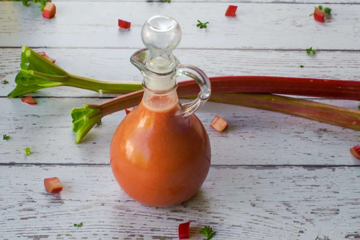 Bottle of Rhubarb Vinaigrette with 2 stalks of rhubarb in the background.