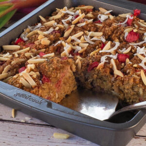A pan of Rhubarb Baked Oatmeal with a pie server wedged under a piece, where 2 pieces are missing.