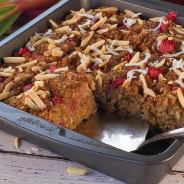 A pan of Rhubarb Baked Oatmeal with a pie server wedged under a piece, where 2 pieces are missing.
