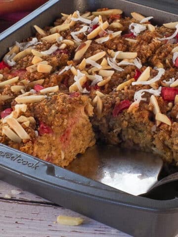 A pan of Rhubarb Baked Oatmeal with a pie server wedged under a piece, where 2 pieces are missing.