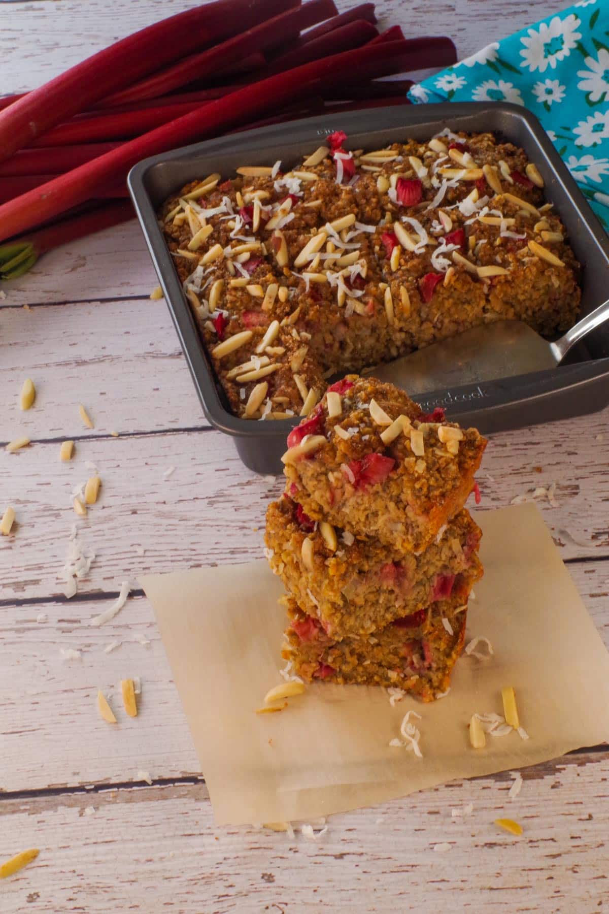 3 pieces of Rhubarb Baked Oatmeal piled on top of each other, on a piece of parchment paper with more Baked Rhubarb Oatmeal in the background.