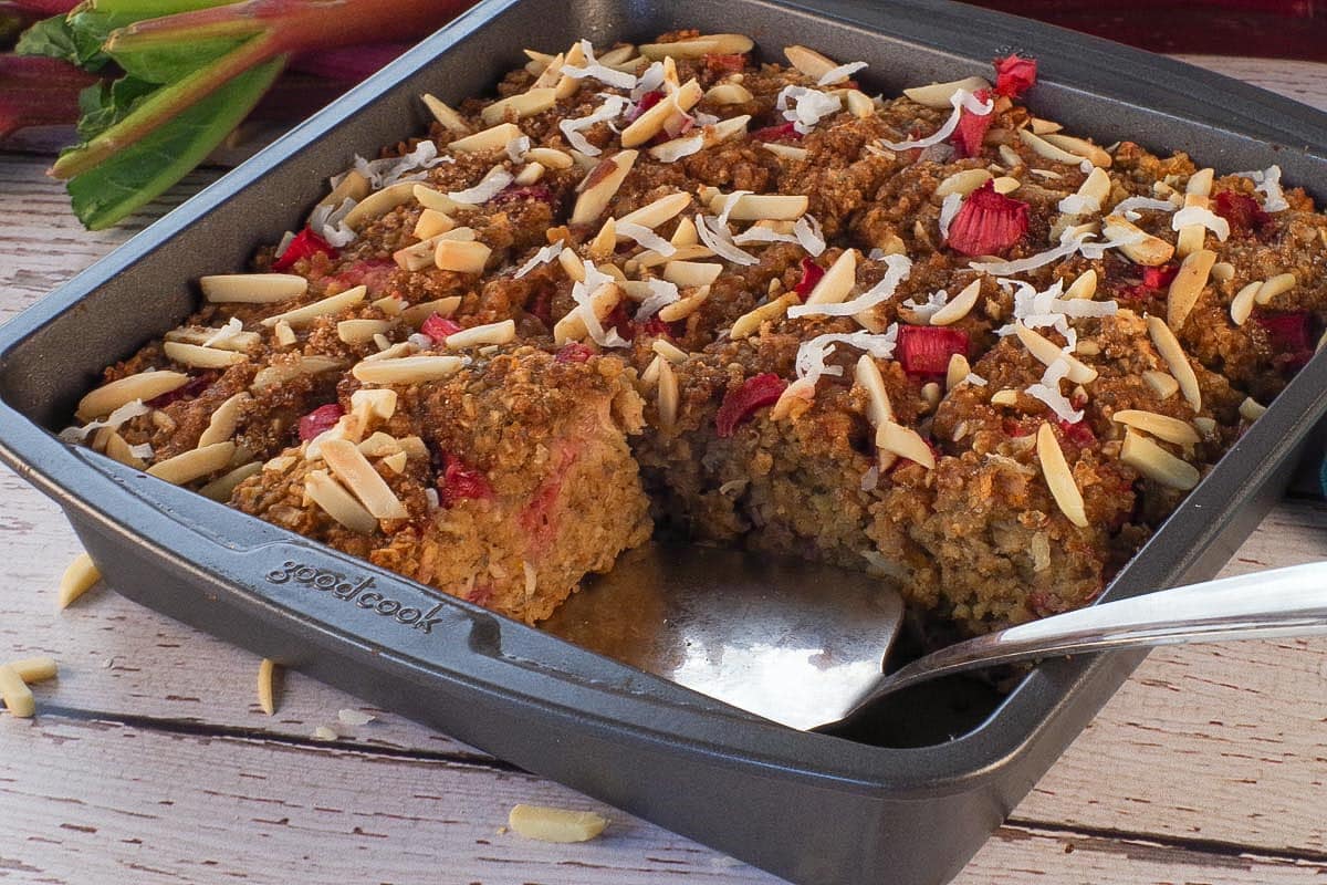 A pan of Rhubarb Baked Oatmeal with a pie server wedged under a piece, where 2 pieces are missing.