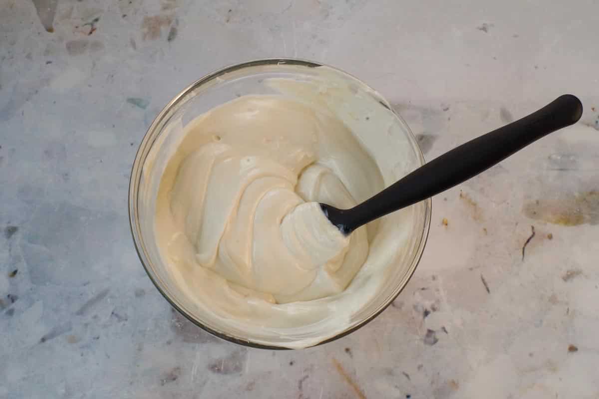 Greek yogurt mixed with vanilla and agave syrup in a medium glass bowl, with a black spatula.