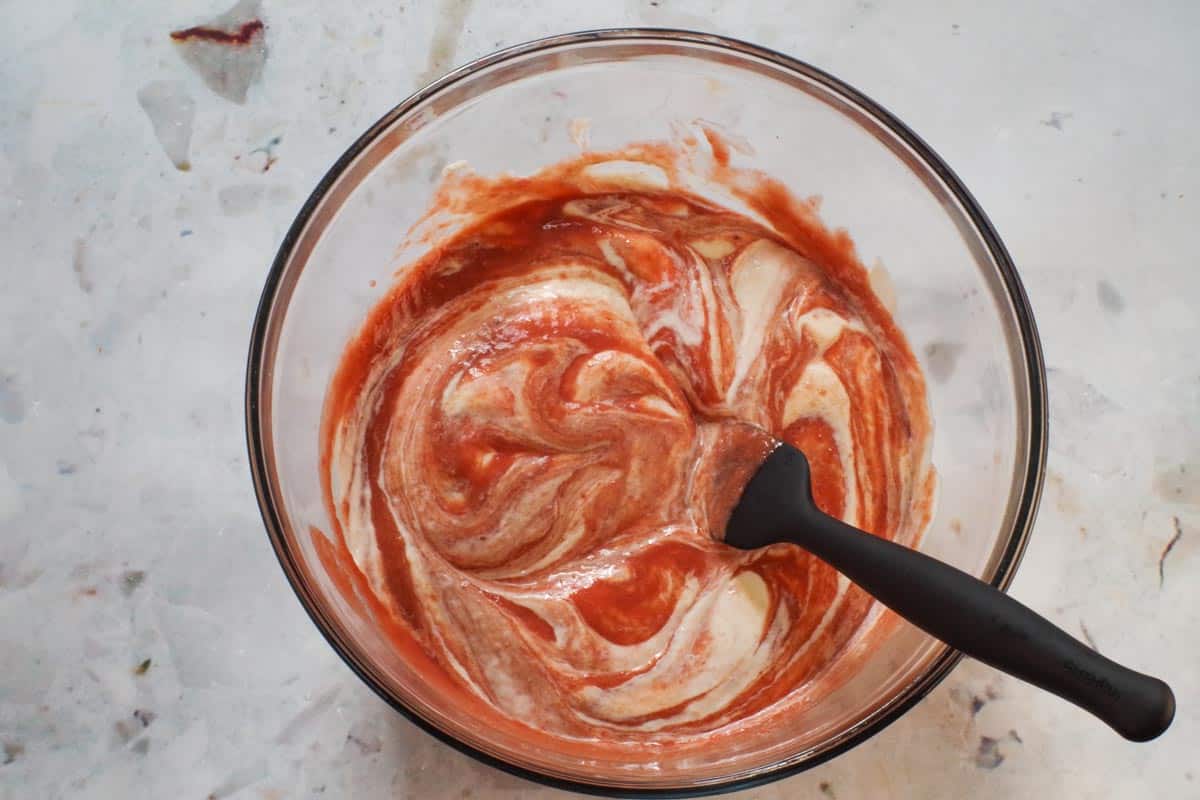 Yogurt and rhubarb puree mixed together again (folded over again) in large glass bowl with black spatula.