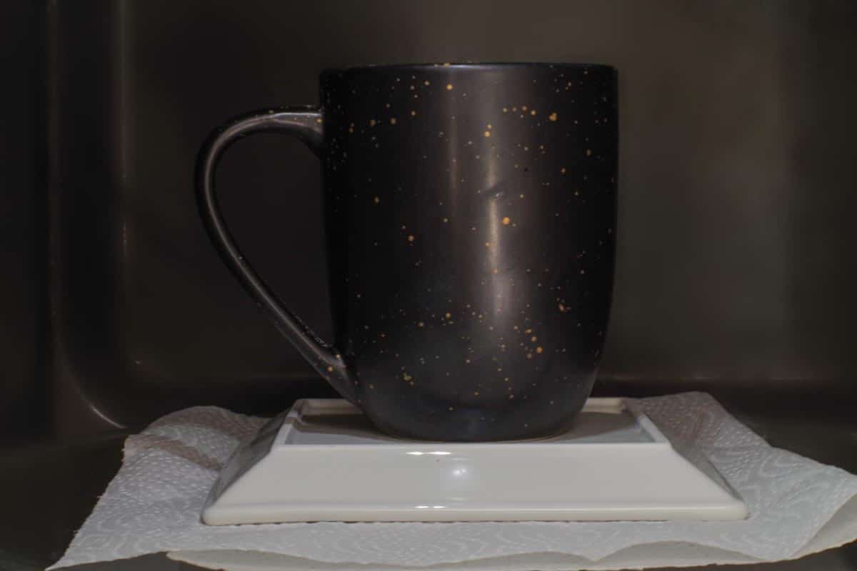 Mug elevated on plate with paper towel underneath plate, in microwave.
