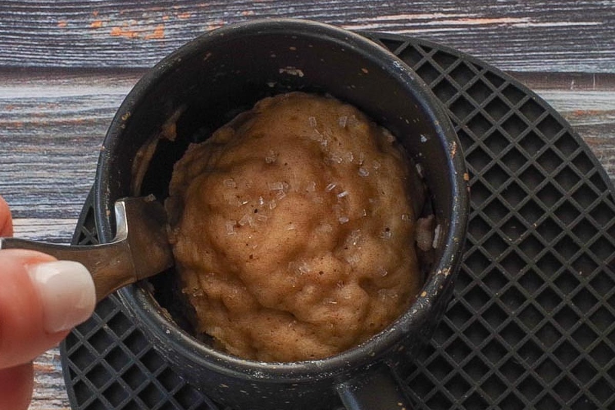 Butter knife being run around the edge of the rhubarb muffin in a mug.