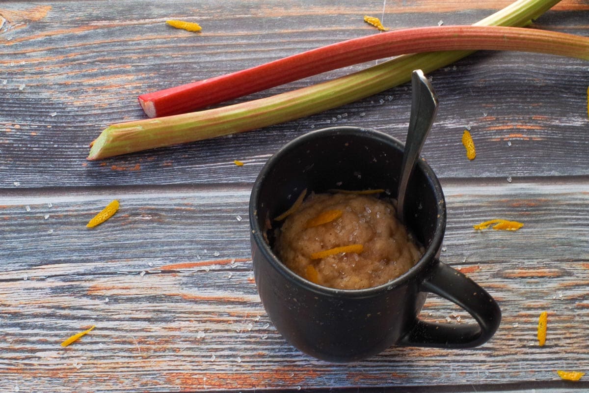 Rhubarb Muffin in a mug garnished with grated orange, with 2 pieces of rhubarb in the background.
