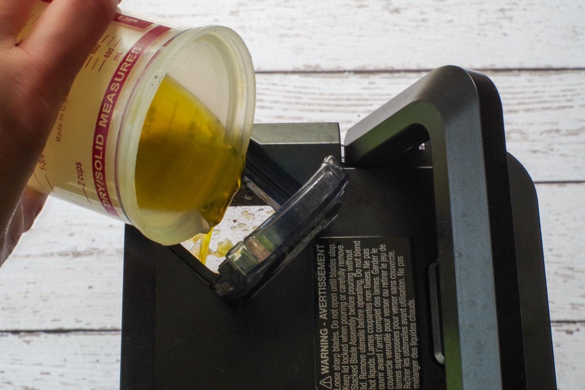 Olive oil being poured in slowly through the top of the blender lid.