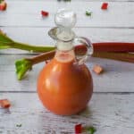 Bottle of Rhubarb Vinaigrette with 2 stalks of rhubarb in the background.