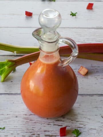 Bottle of Rhubarb Vinaigrette with 2 stalks of rhubarb in the background.