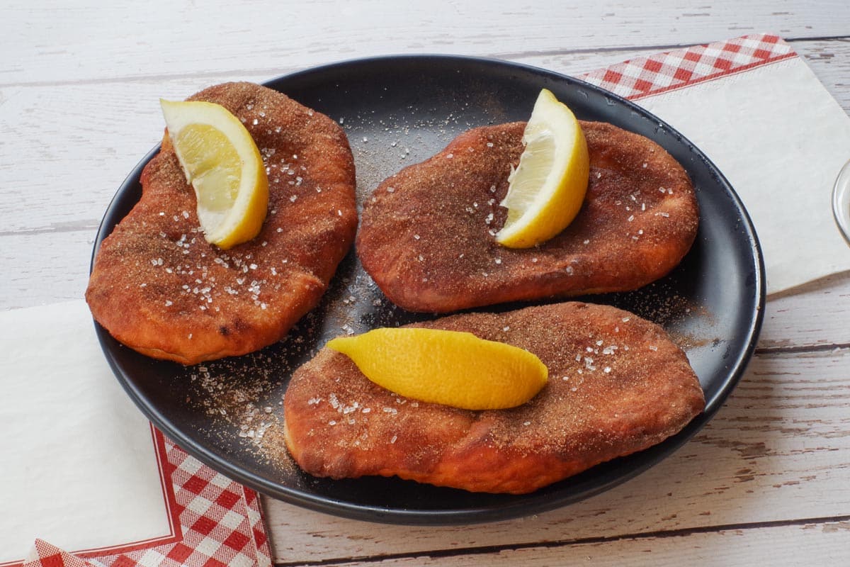3 healthy air fryer beaver tails garnished with lemon wedges. on a black plate with red and white checkered napkins around the plate.