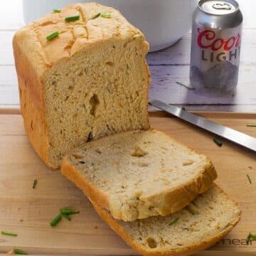 A loaf of Bread Machine Beer Bread on a cutting board, with 2 slices cut and a can of beer in the background
