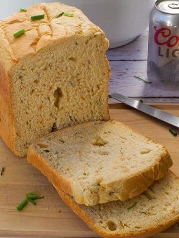 A loaf of Bread Machine Beer Bread on a cutting board, with 2 slices cut and a can of beer in the background