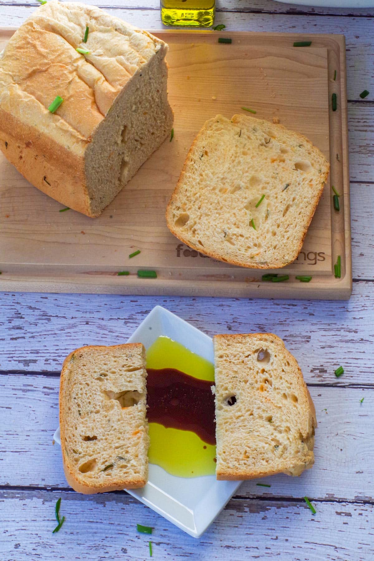 2 pieces of Beer, Cheese and Chive Bread on a white plate with oil and vinegar and more bread on the cutting board.