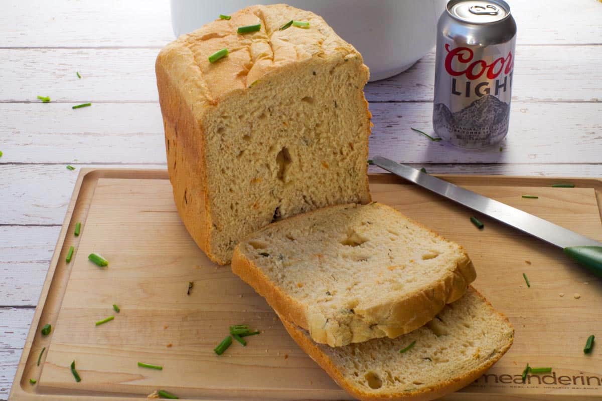 A loaf of Bread Machine Beer Bread on a cutting board, with 2 slices cut and a can of beer in the background