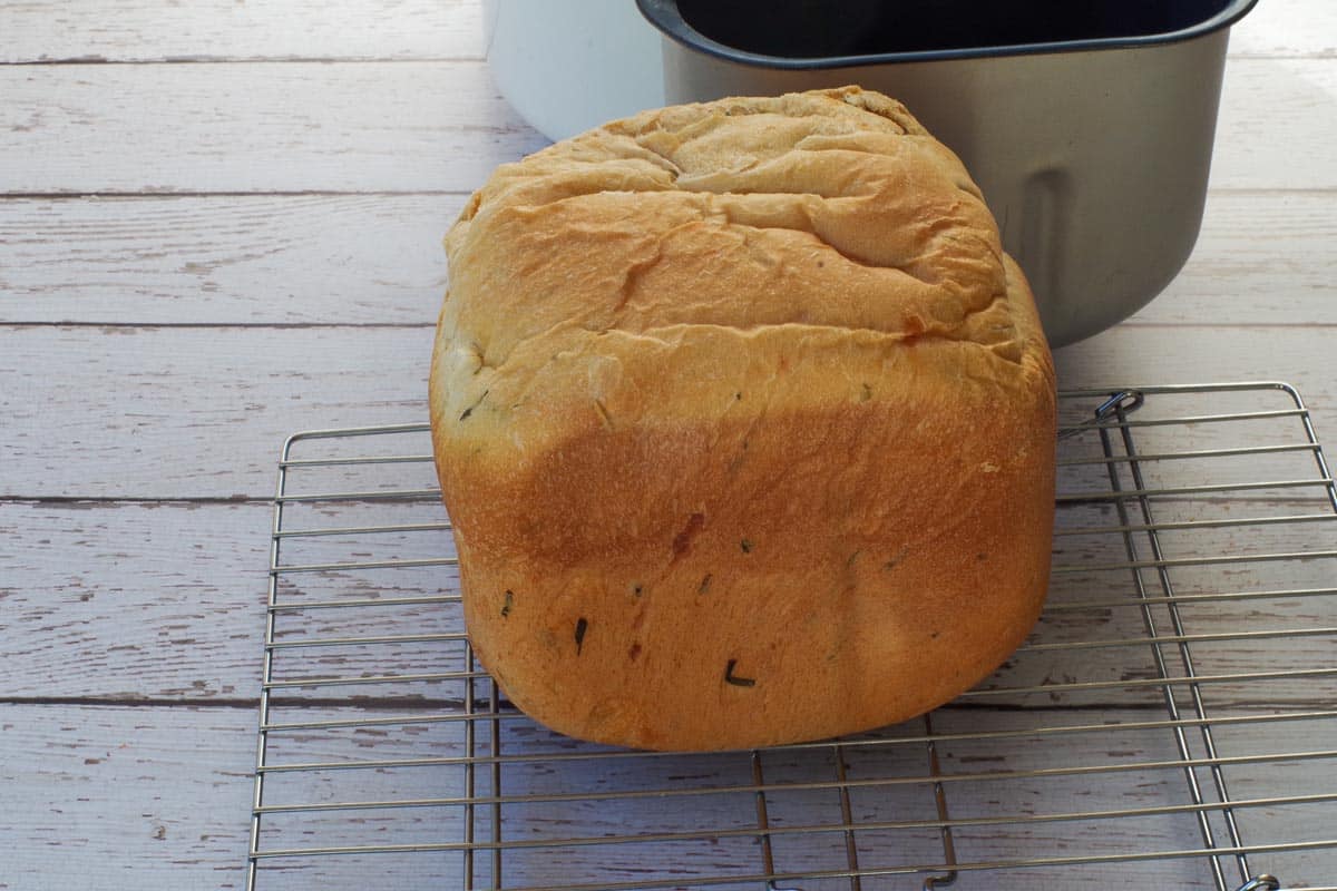 Beer, Cheese and Chive Bread on a cooling rack, with bread machine bread pan in background.