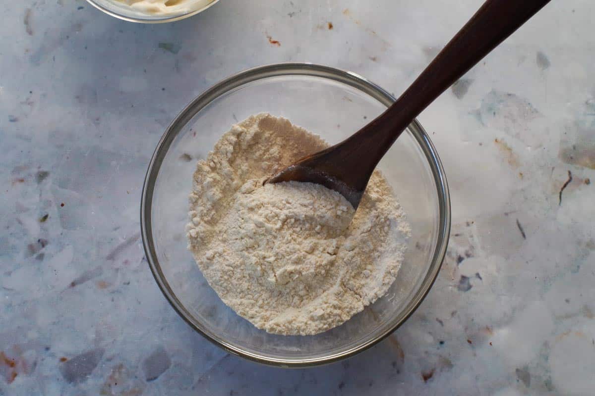 Dry ingredients for Healthy Beaver Tails dough mixed together in glass bowl with wooden spoon.