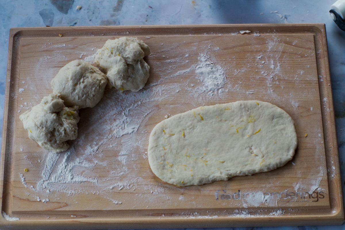 1 section of dough rolled into a beaver tail and 3 sections on the side of a wooden cutting board.
