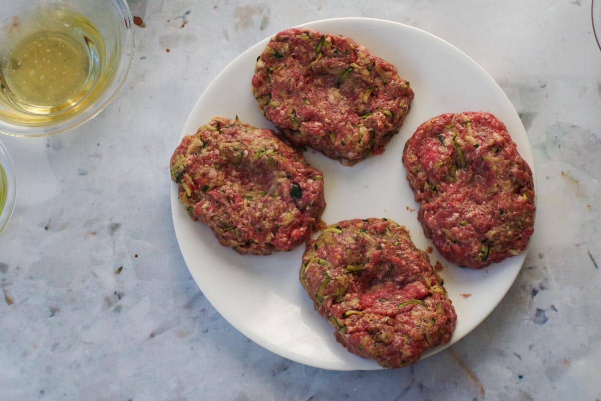 4 oval shaped Salisbury Steak patties on a white plate.