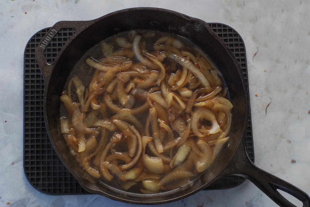 Beer and broth poured into sauteed onions for Salisbury steak gravy in black cast iron frying pan.