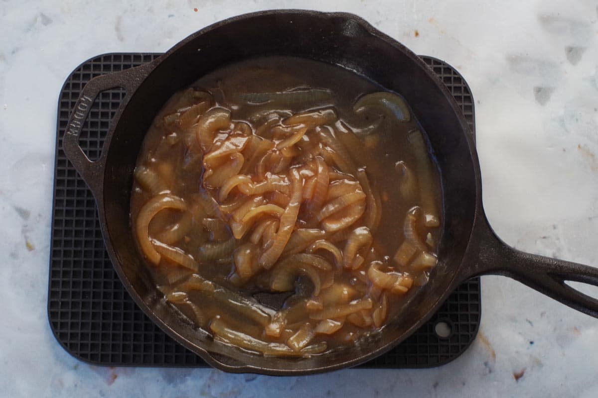 Cornstarch and water mixed into onion, beer and broth mixture, in cast iron frying pan, to create thickened gravy for Healthy Salisbury steaks.