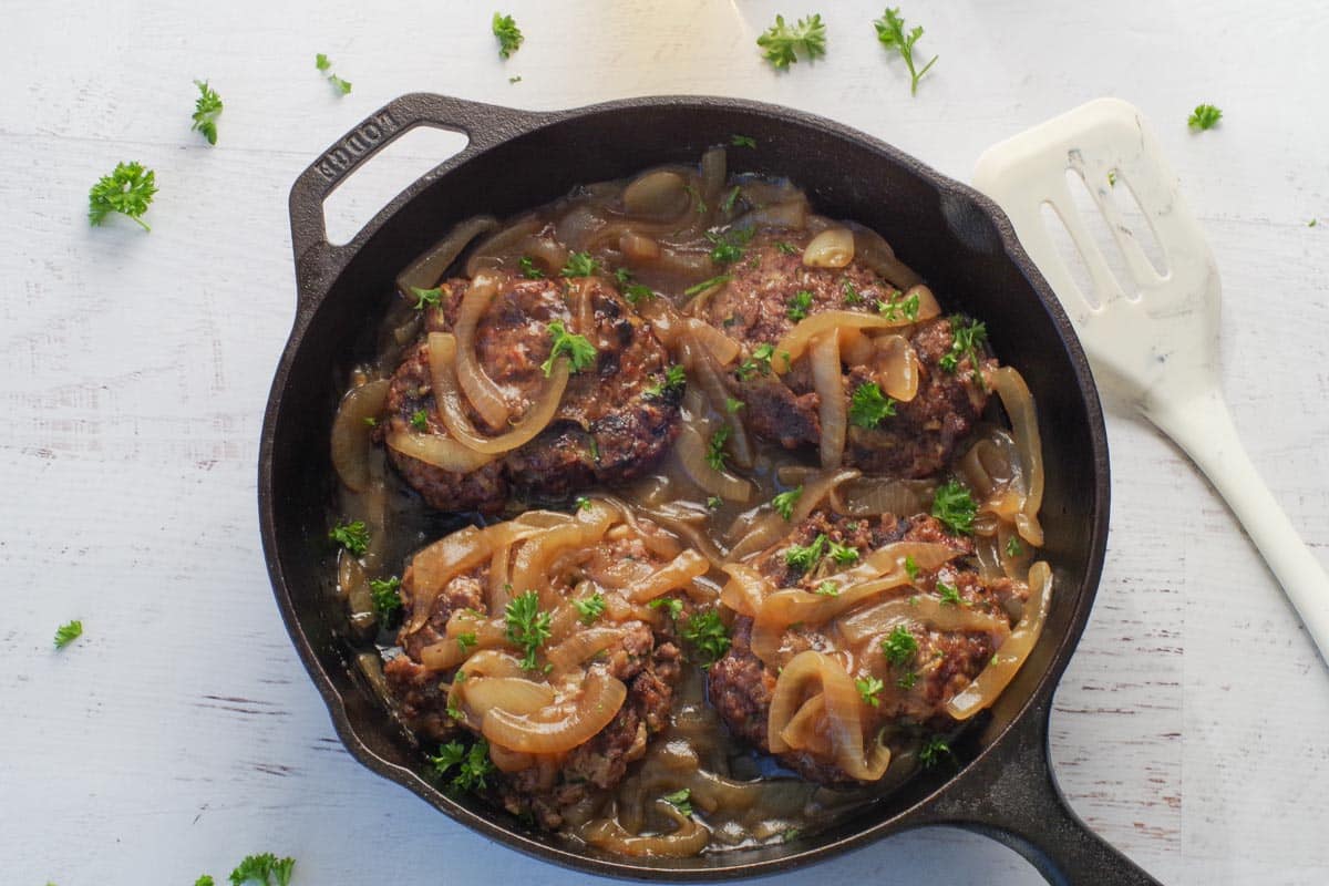 Beer and Onion Gravy over Healthy Grilled Salisbury Steaks in a black cast iron frying pan.