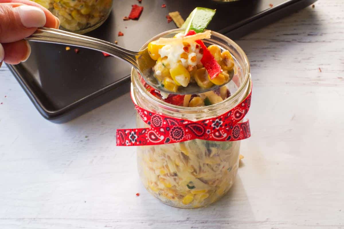 Healthy Mexican Street Corn Cups with some street corn being held up on a spoon over the jar.