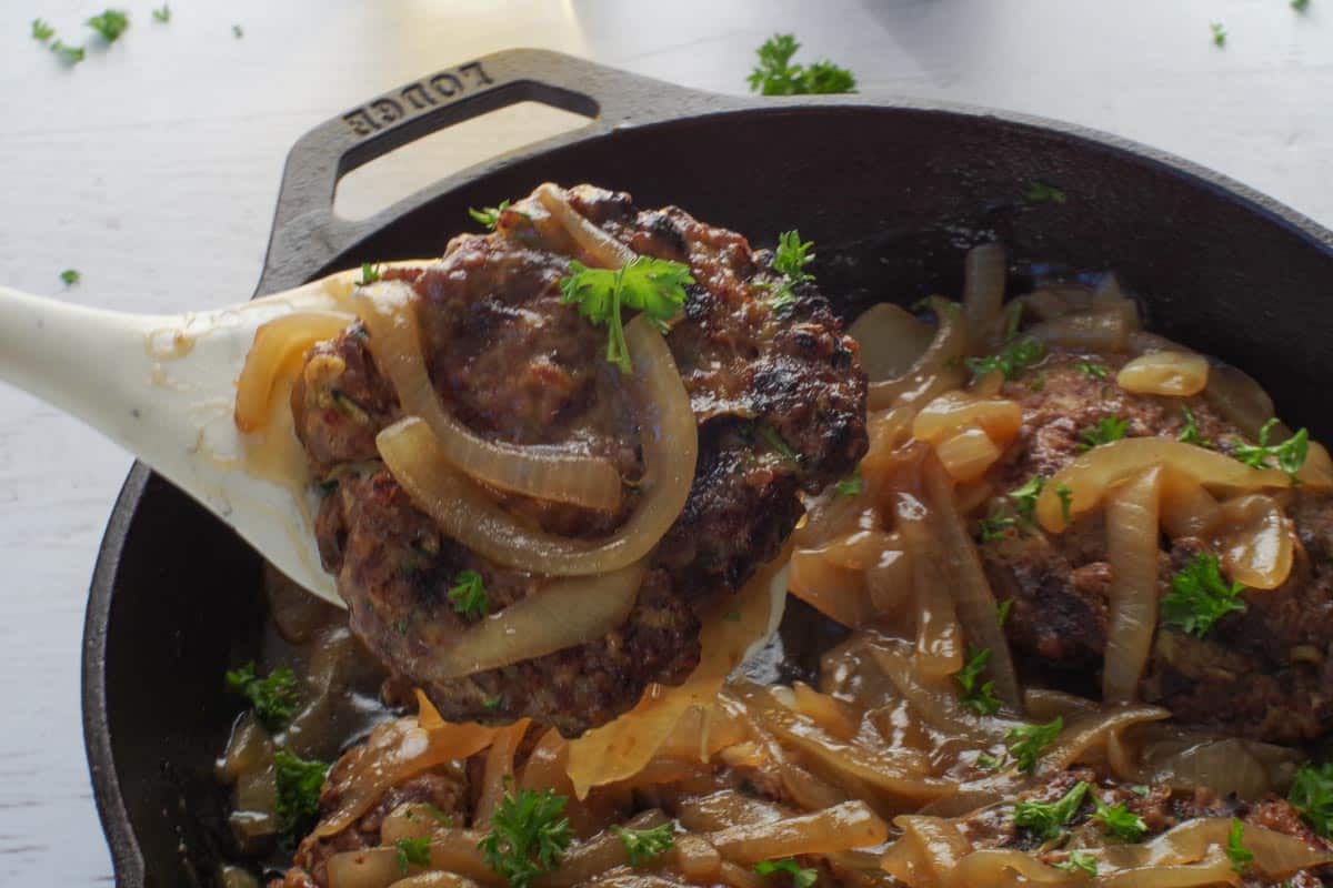 A healthy grilled Salisbury Steak being lifted out of a cast iron pan.