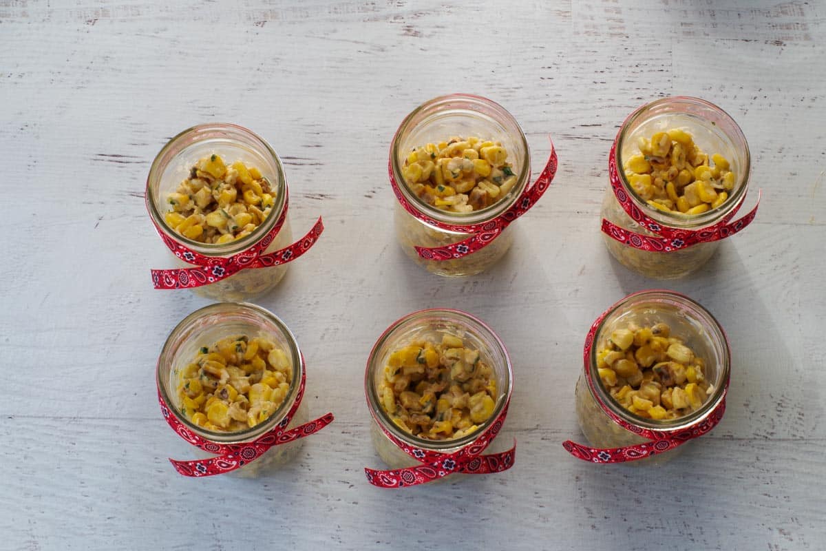 Corn spooned into small mason jars tied with bandana ribbon.