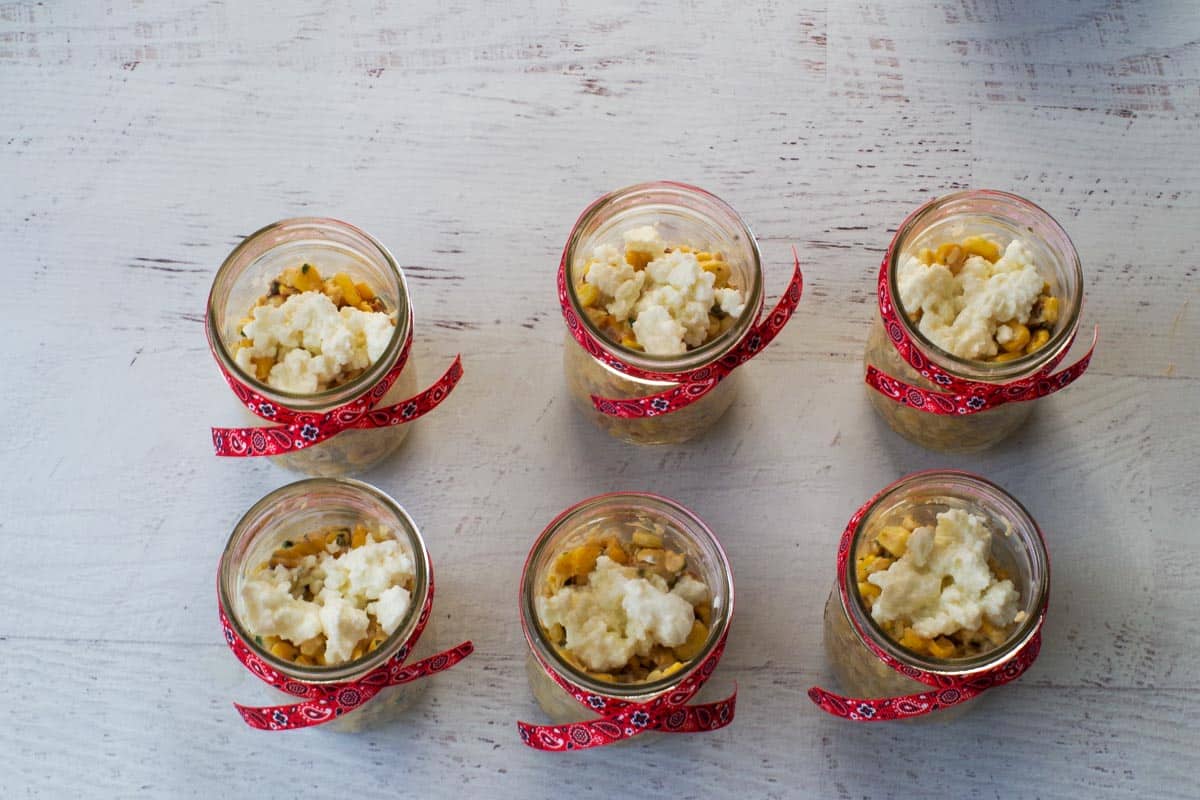Feta cheese added on top of corn in jars.