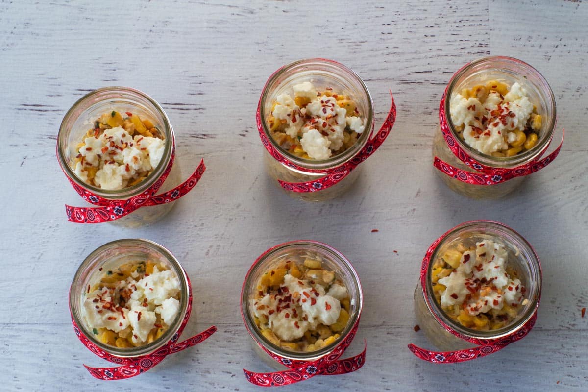 Crushed red pepper flakes sprinkles over feta cheese in jars.