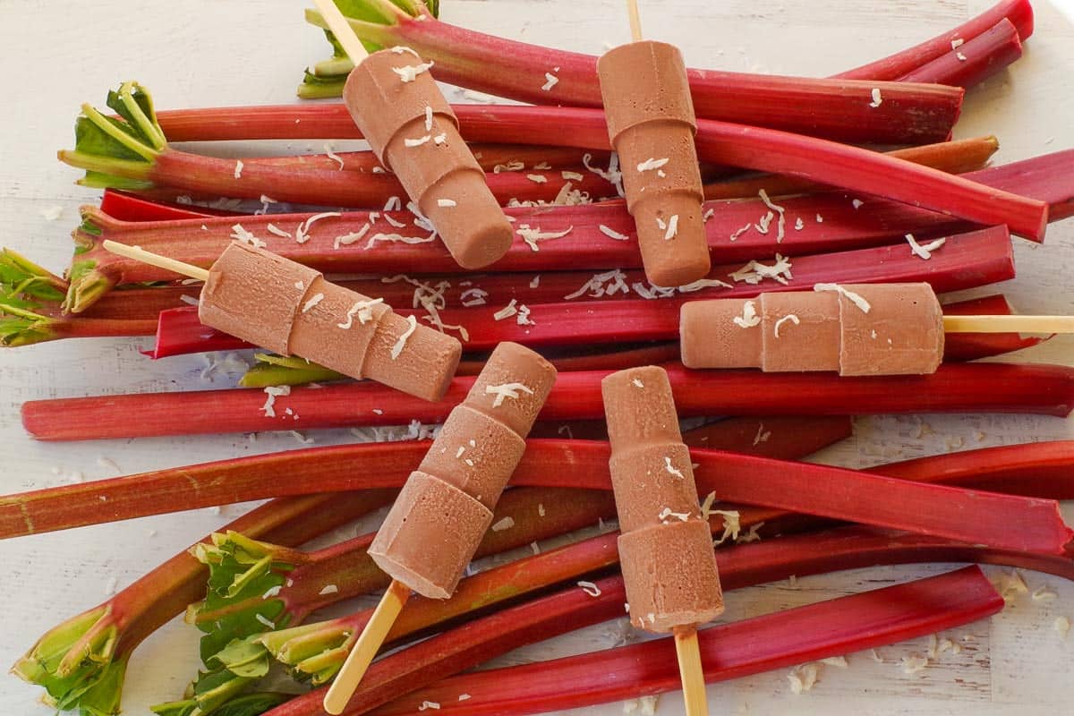 A pile of rhubarb with 6 popsicles laying on top and shredded coconut scattered.