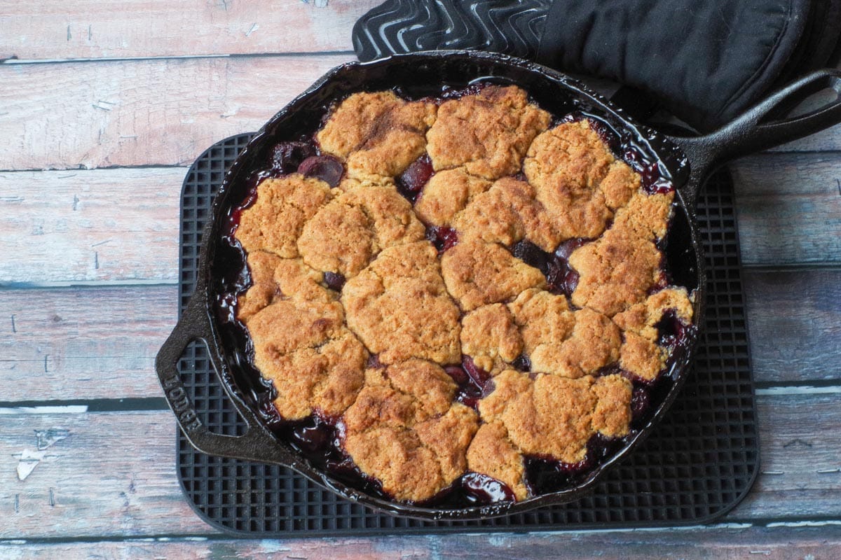 Baked fresh Cherry Cobbler in a skillet on a rectangular trivet.