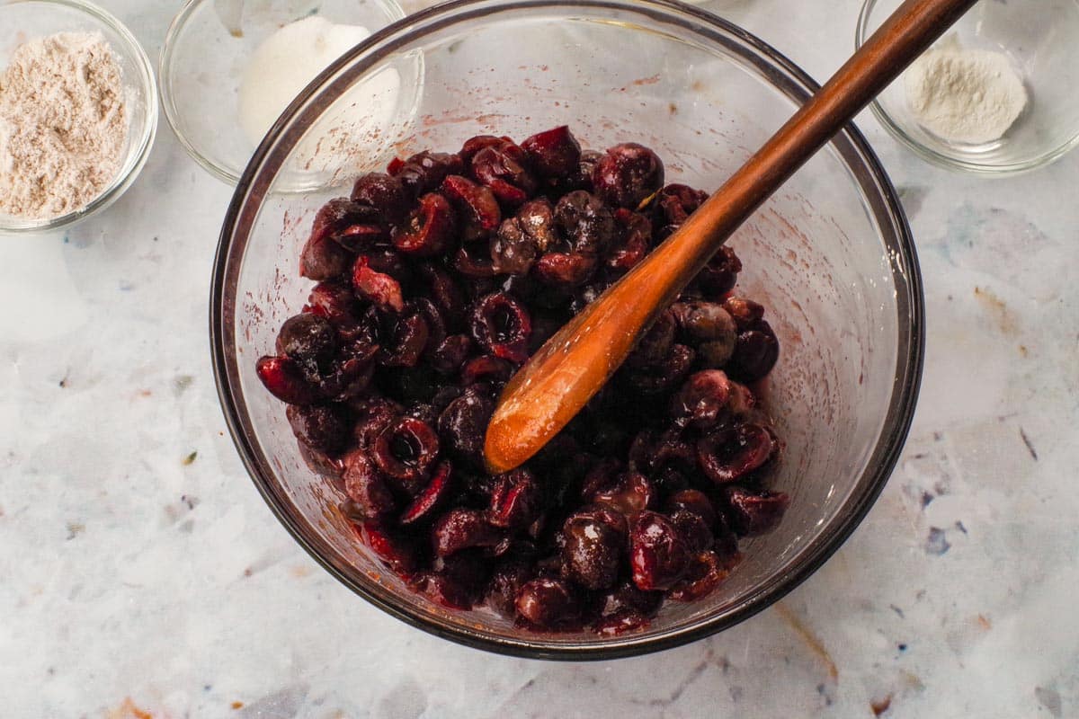 Cherries in a large glass bowl, mixed with cinnamon, cornstarch, lemon, almond extract and sugars,
