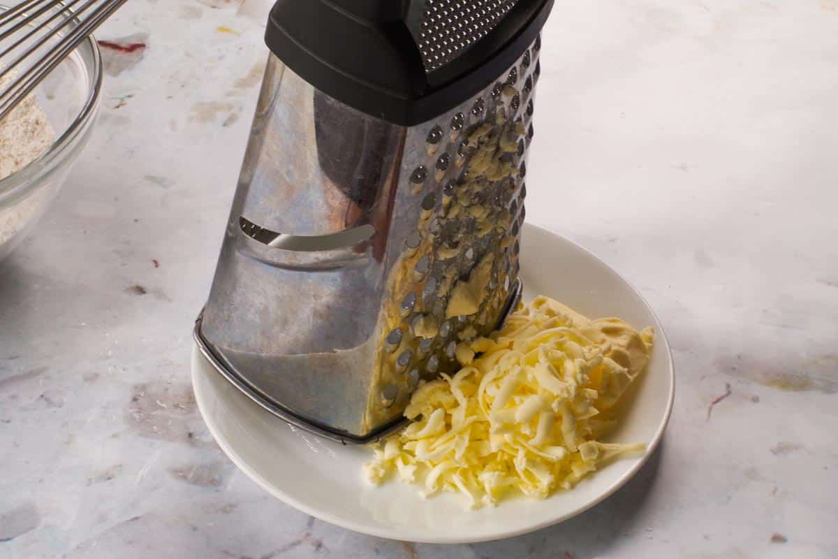 Grated butter on a plate beside a box grater.