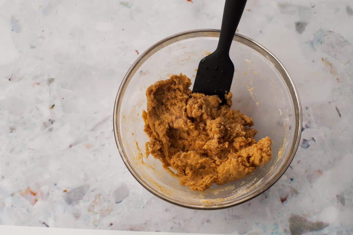 Hot water mixed into the dry mixture in a glass bowl, with a black silicone spatula.