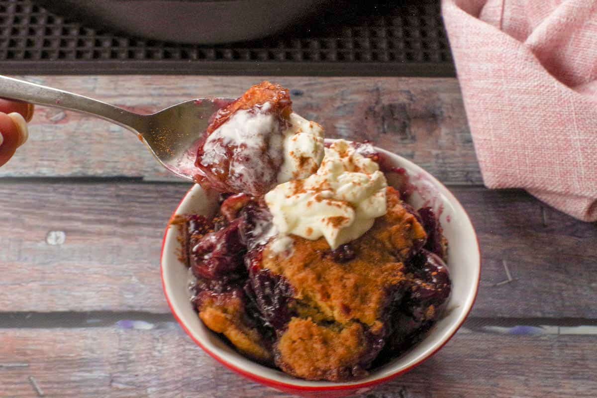 Fresh Cherry Skillet Cobbler being held up on a spoon over a bowl of more fresh cherry skillet cobbler.