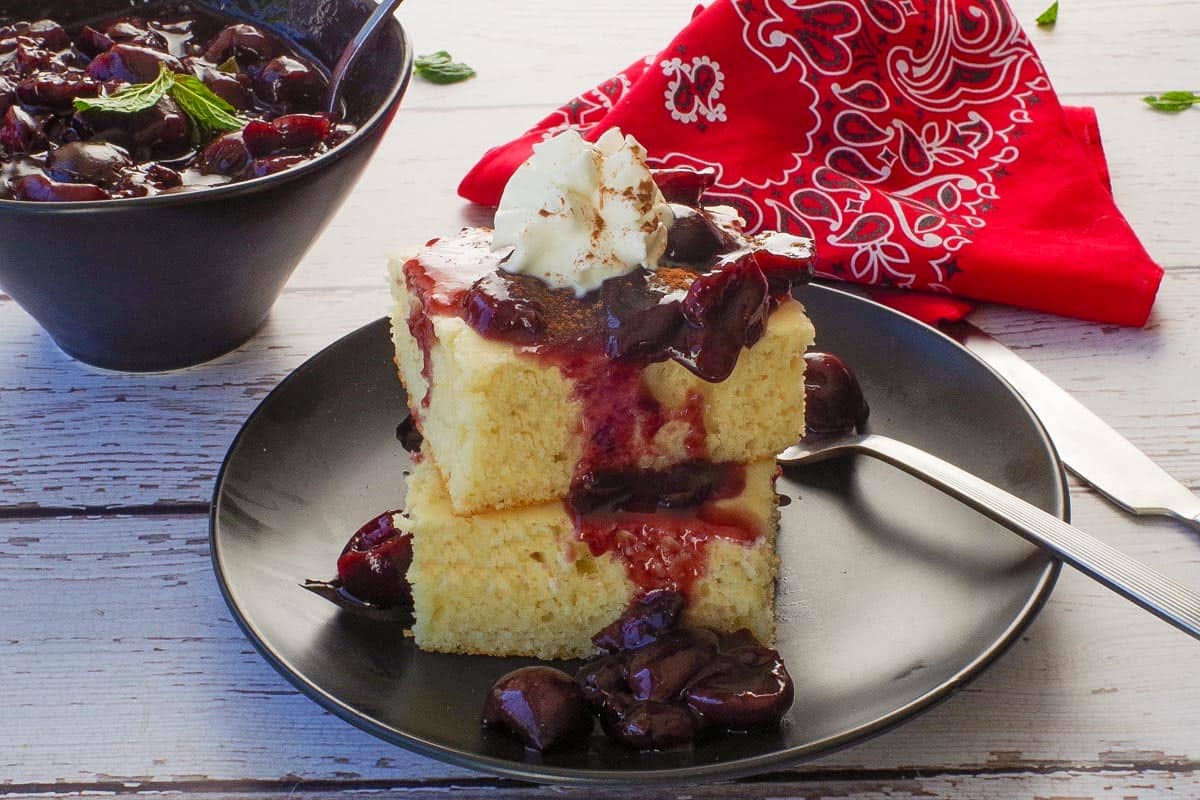 Fresh Cherry Sauce poured over 2 stacked oven baked pancakes with more cherry sauce in the background.