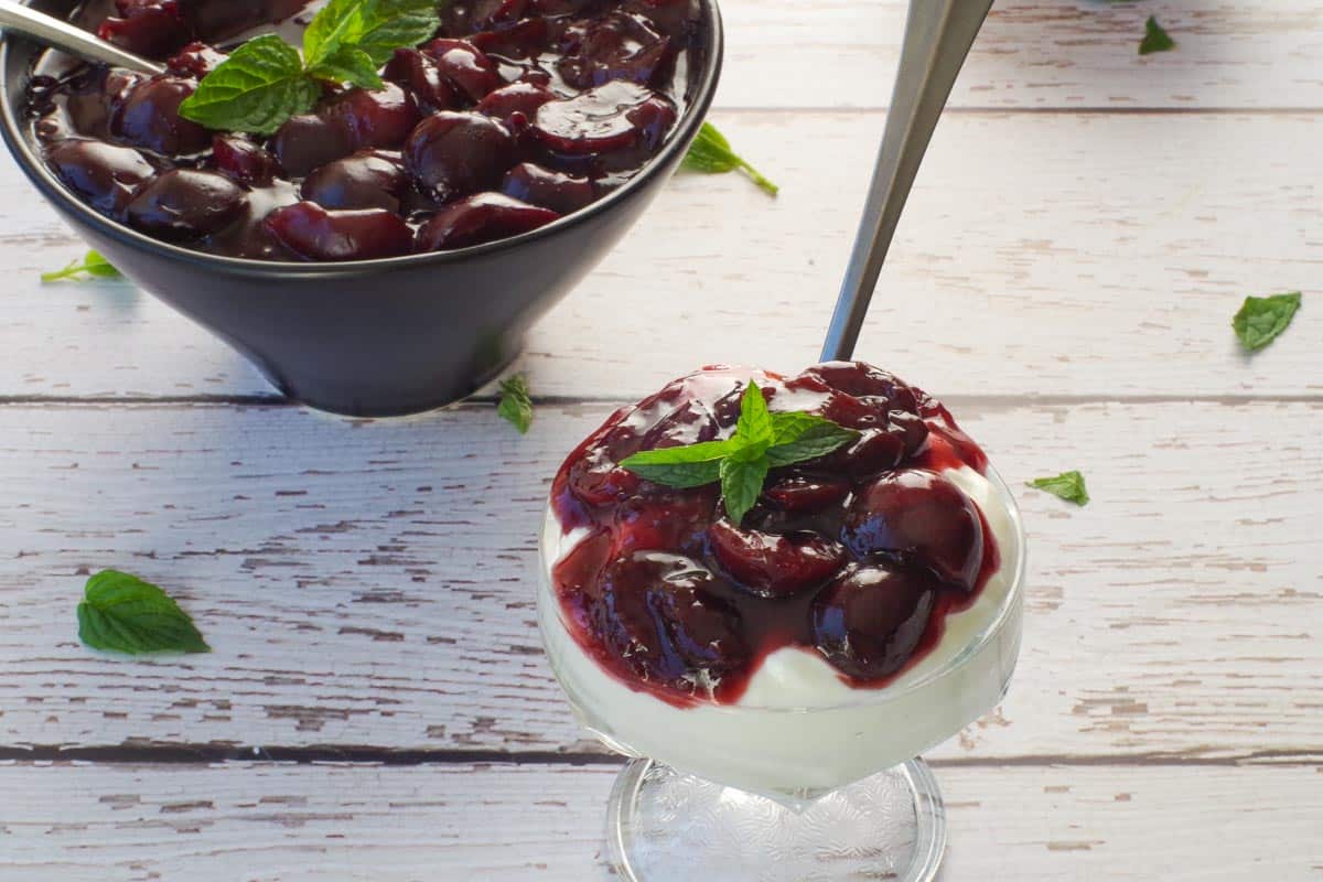 Healthy Fresh Cherry Sauce poured over a dish of Greek Yogurt with a bowl of more fresh cherry sauce in the background.