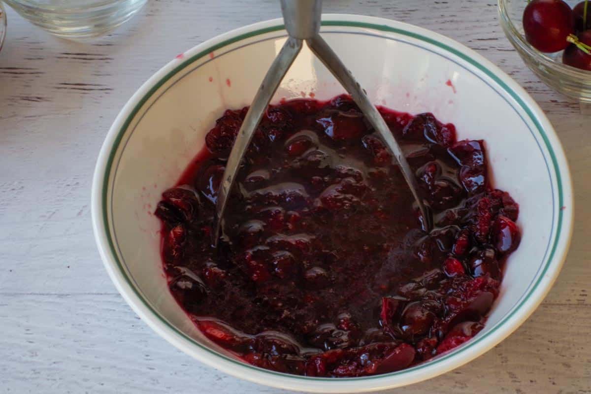 Cherries being mashed in a white bowl.