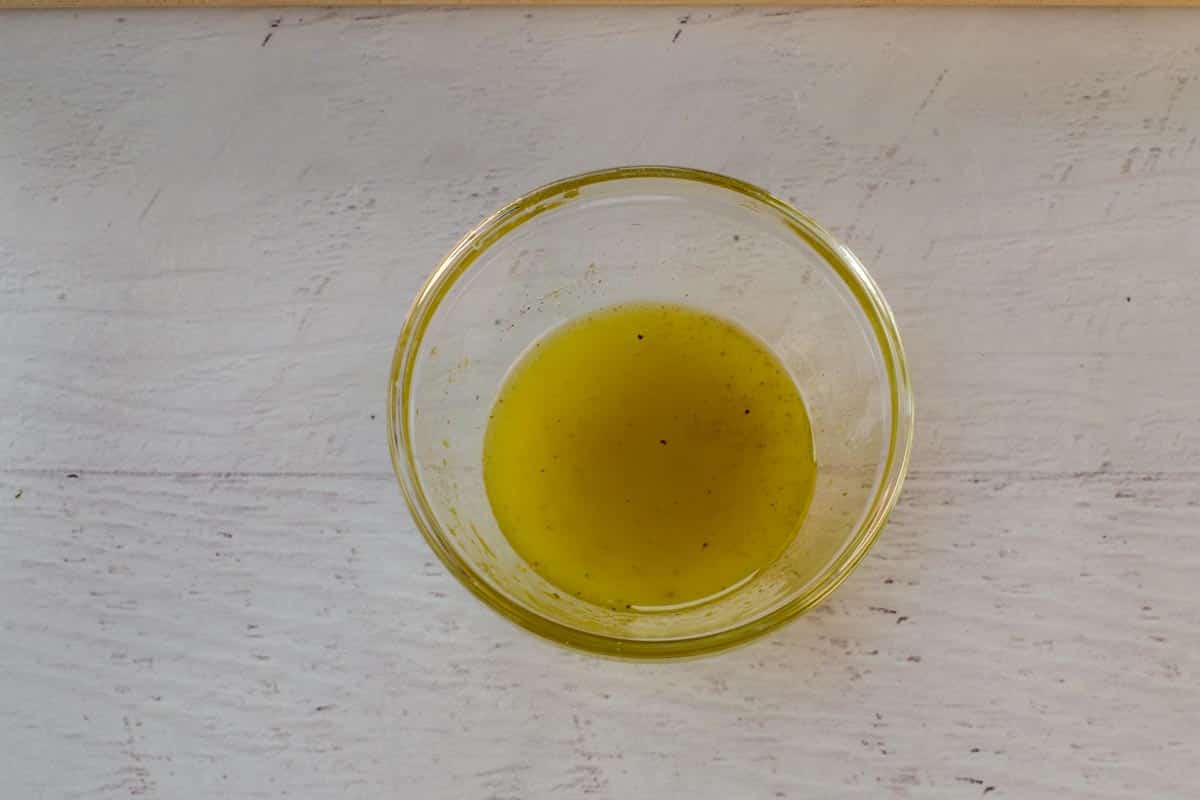 Oil and lemon juice mixed with salt and pepper in a glass bowl.