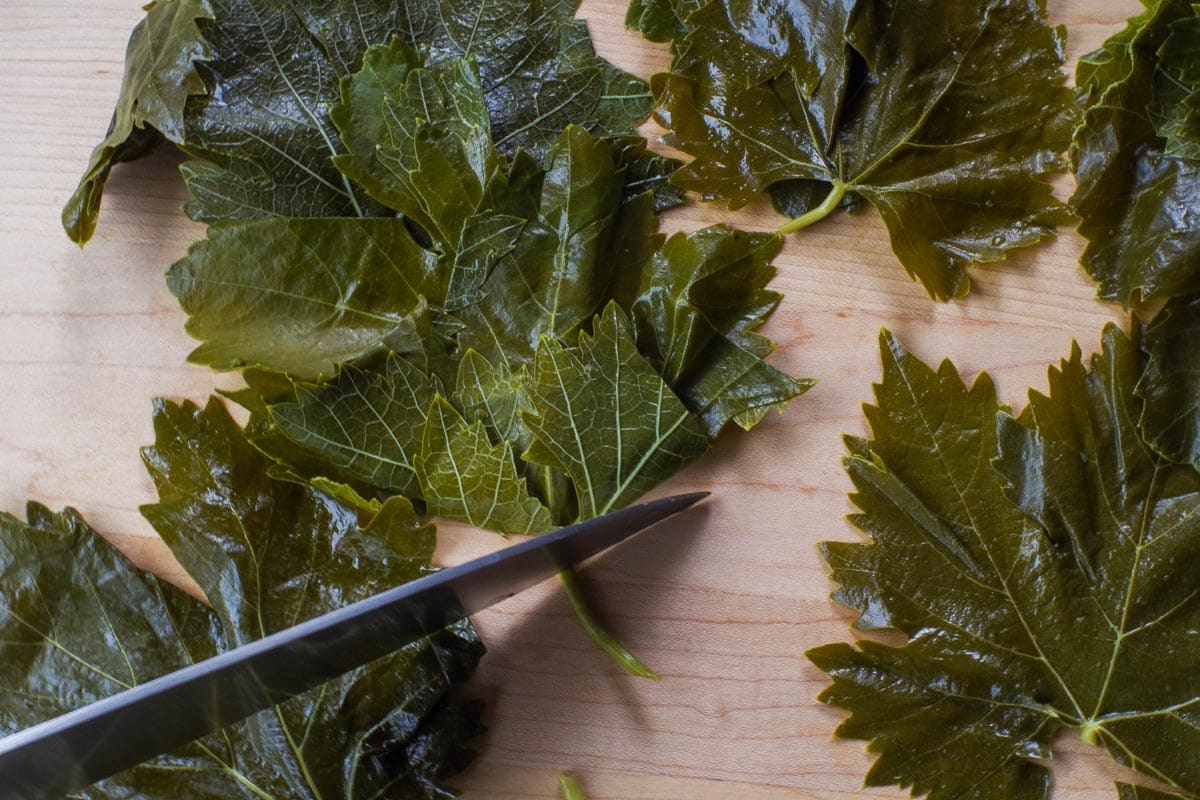 Tough stems being cut off grape leaves on cutting board.
