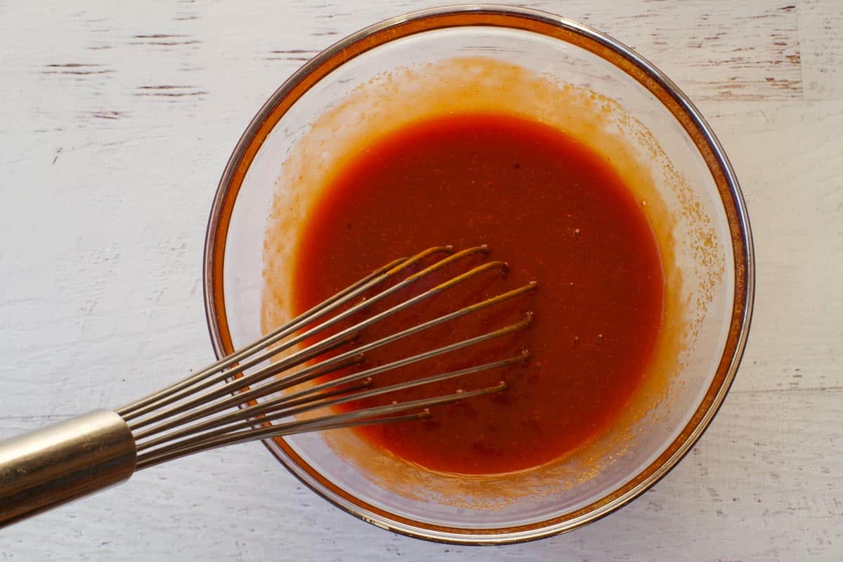 Marinade ingredients mixed in a large glass bowl with a whisk.