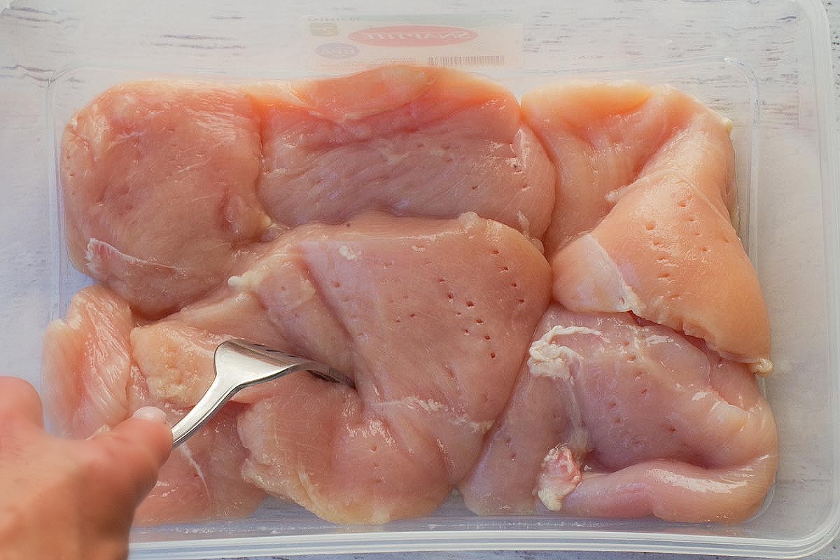 Chicken being perforated with a fork in a container.